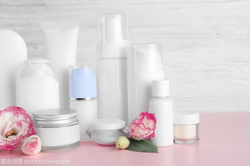 不同的化妝品瓶和灰色墻上背景上的花朵